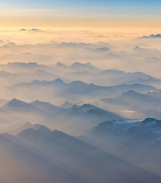 Mountain range peaks emerge from clouds at sunrise.